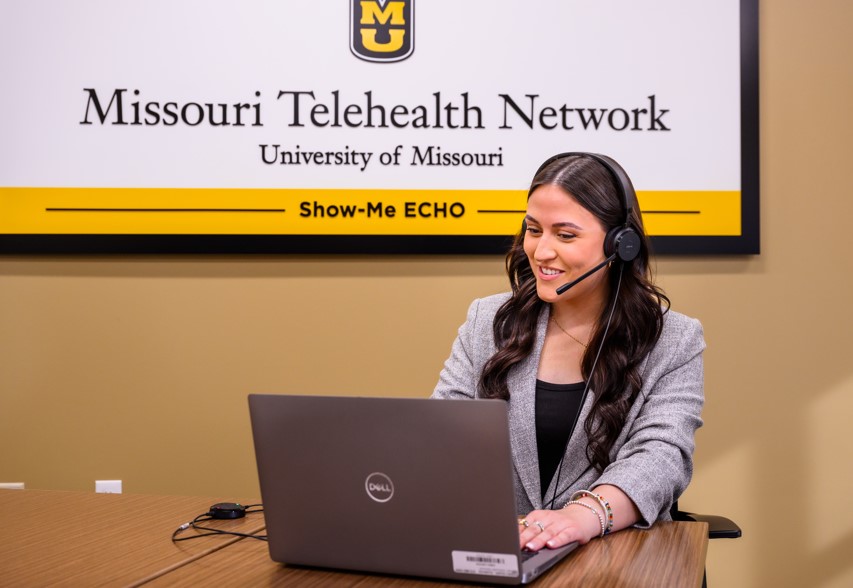 A smiling employee sits at a computer laptop wearing a headset.