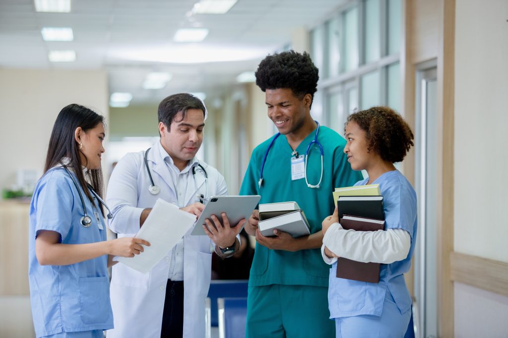 Image of a doctor inside a clinical setting holding a tablet and showing three other medical professionals/students what's on it.